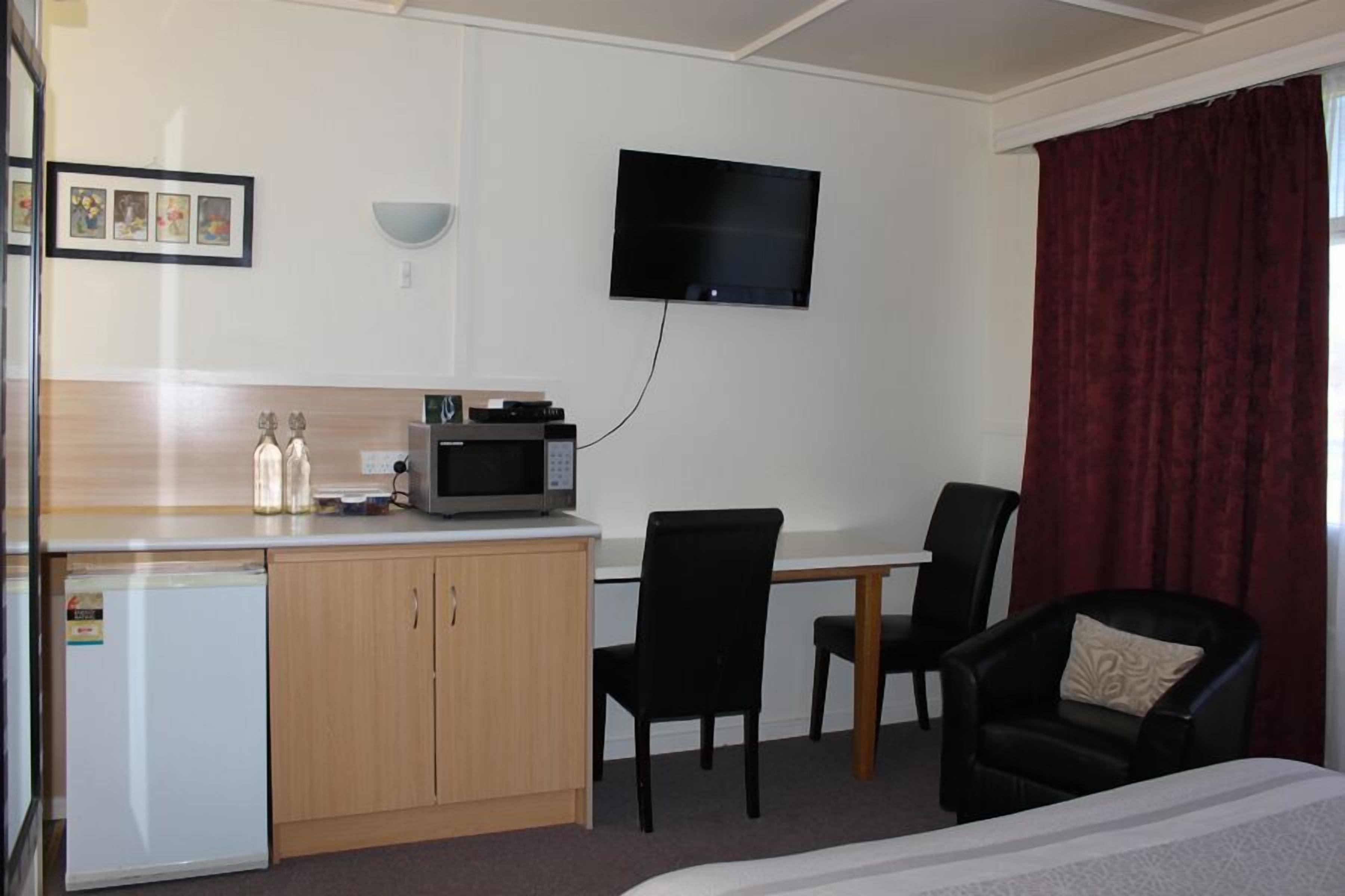 A hotel room with a bed, a desk with a microwave, a chair, a small refrigerator, and a TV mounted on the wall.