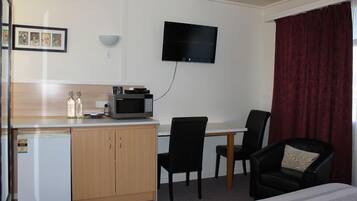 A hotel room with a bed, a desk with a microwave, a chair, a small refrigerator, and a TV mounted on the wall.