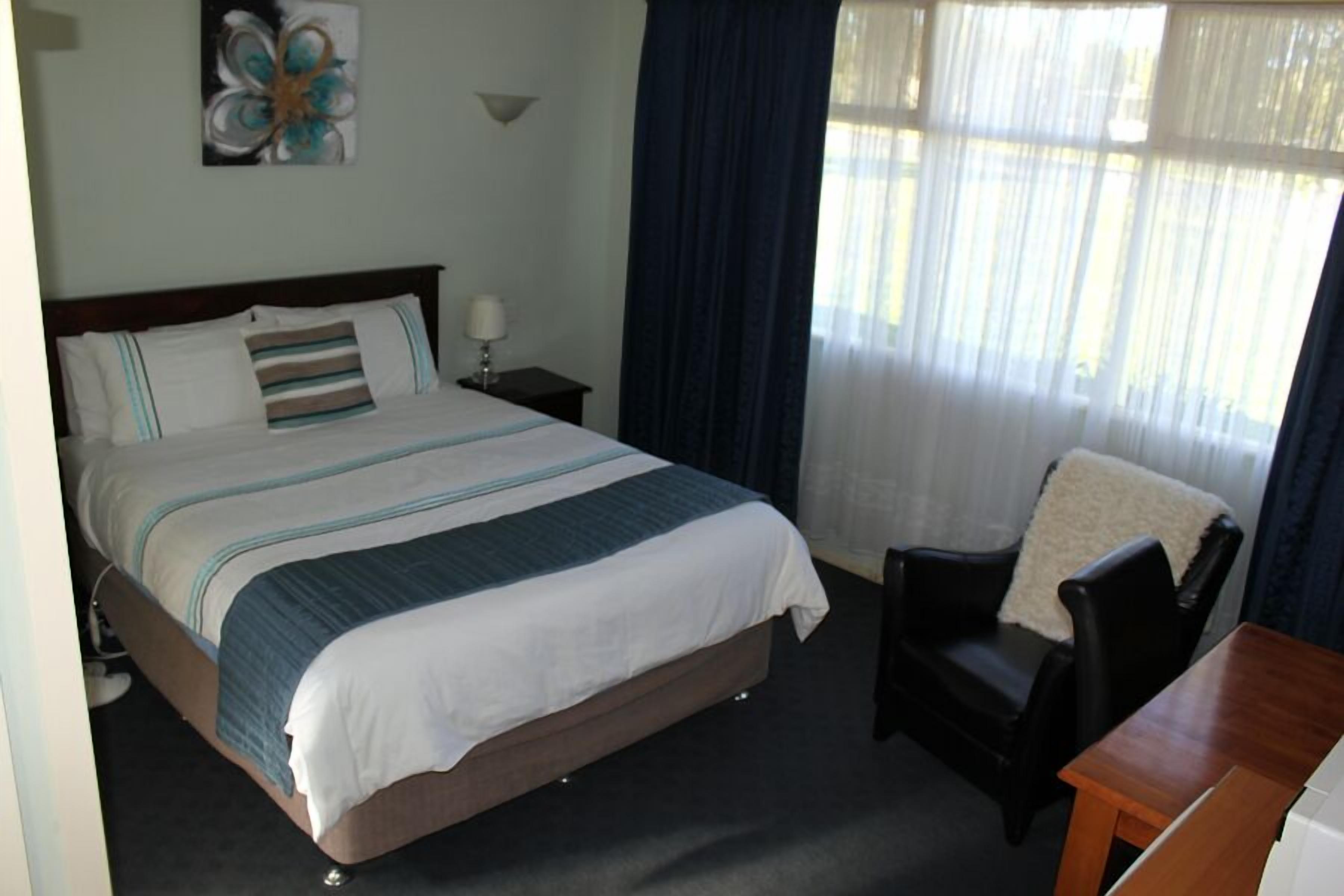 A hotel room with a bed, a chair, a table, and a window with curtains.