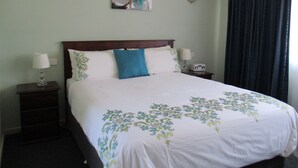 A neatly made bed with a floral bedspread, two bedside lamps, a radio, and a wall art piece above the bed. - Kaniva Midway Motel (Kaniva)
