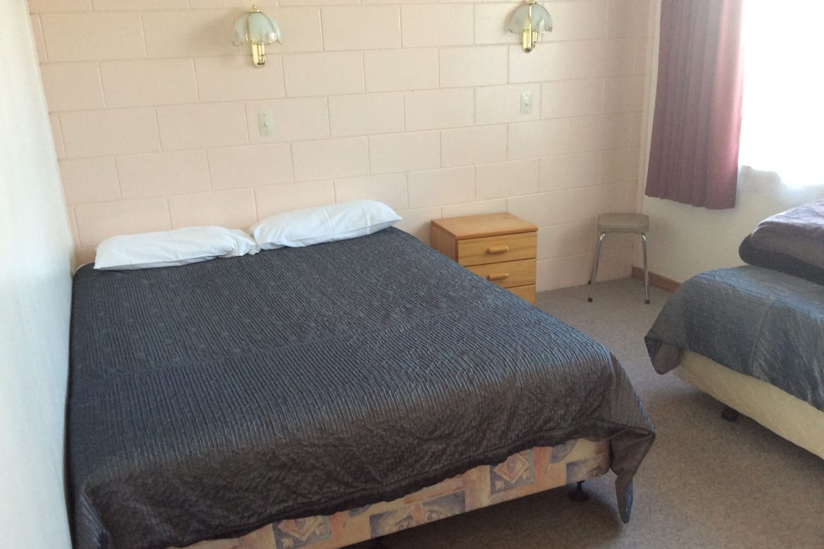 A bedroom with a bed, a nightstand, a chair, and a window with curtains.