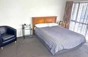 Un dormitorio con una cama individual, una silla, una mesita de noche y un ventanal con cortinas.