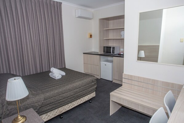 A hotel room with a bed, a desk, a microwave, a small fridge, a lamp, and a mirror.