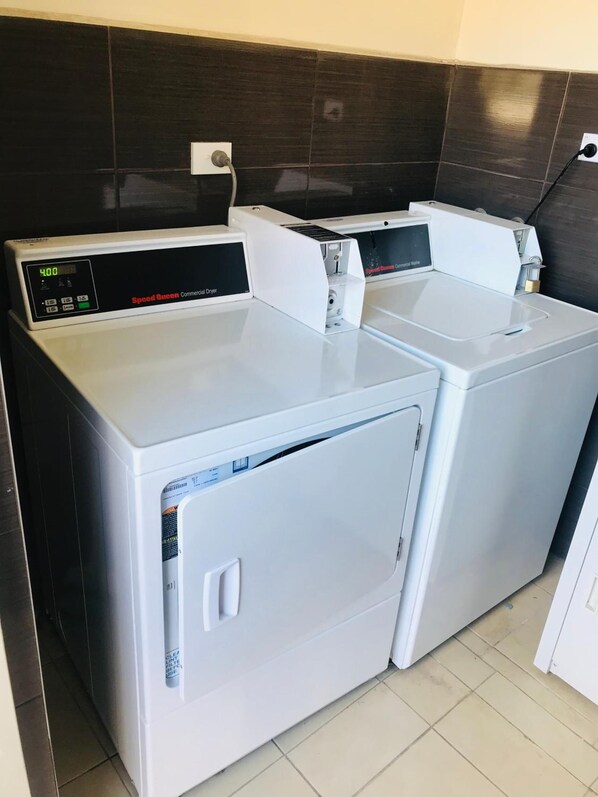A commercial dryer with a digital display and a control panel, located in a room with dark tiled walls and a tiled floor. - Westside Motor Inn (Ashfield)