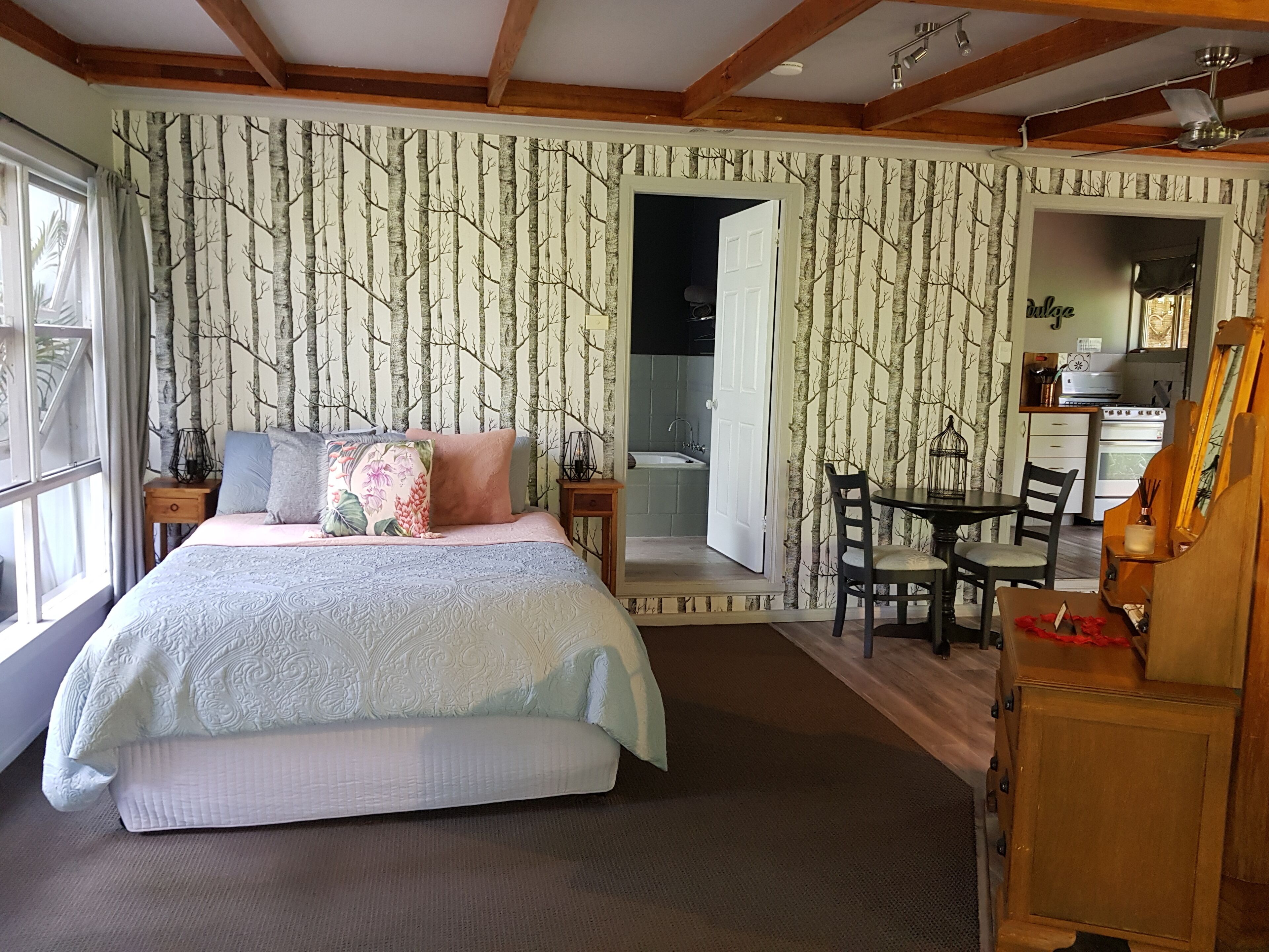 Un dormitorio con cama, escritorio, silla, mesa de comedor y vista al baño.