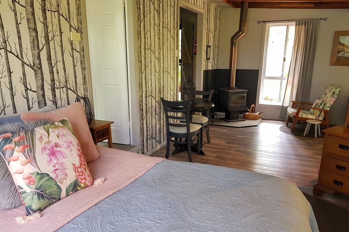 A bedroom with a bed, a chair, a table, a fireplace, and a window.