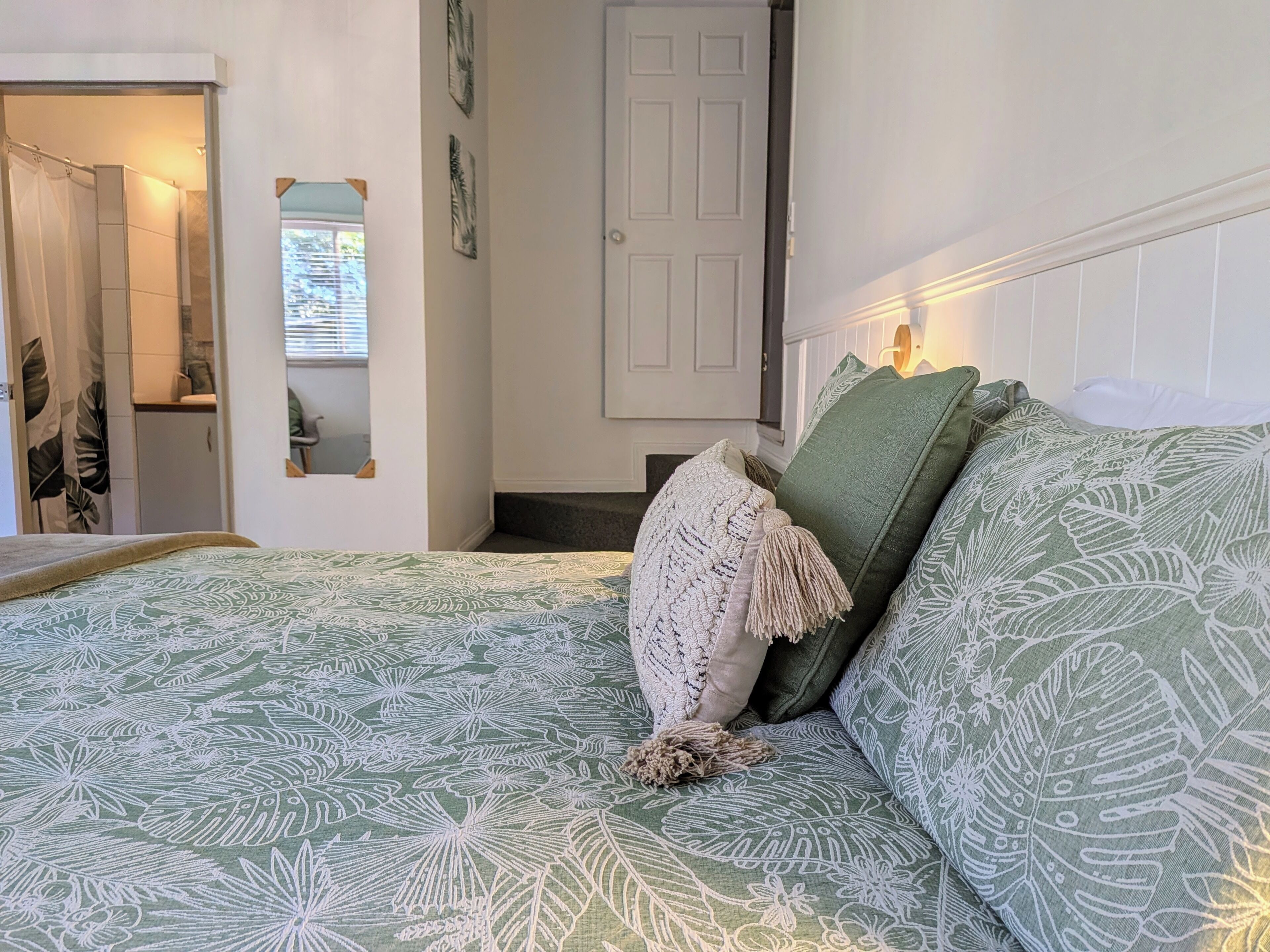 A bedroom with a bed, a door, a mirror, and a window.