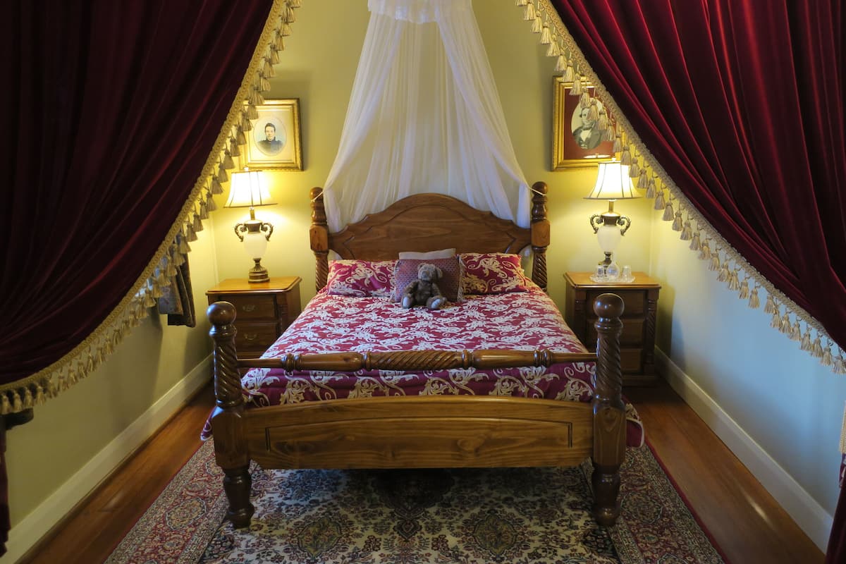 Ein Bett mit Baldachin, zwei Nachttischlampen, ein gemustertes Teppich und ein Holz-Kopfstück.