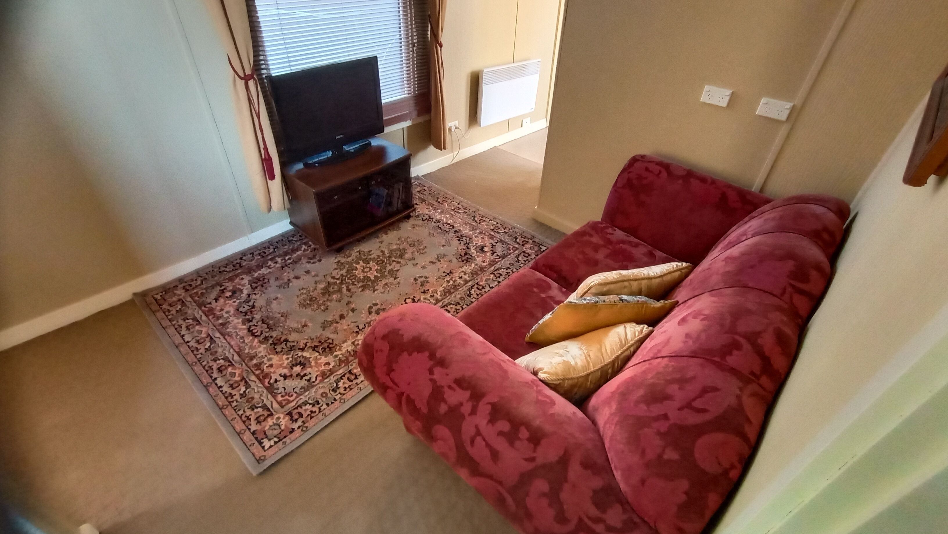 A living room with a red sofa, a patterned rug, a flat-screen TV, and a wall-mounted heater.
