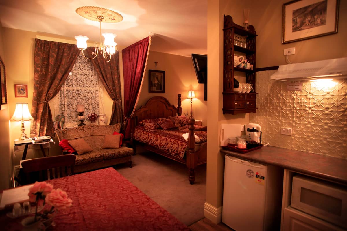 Ein Schlafzimmer mit Bett, Nachttisch, Lampe und einer kleinen Küchenzeile.