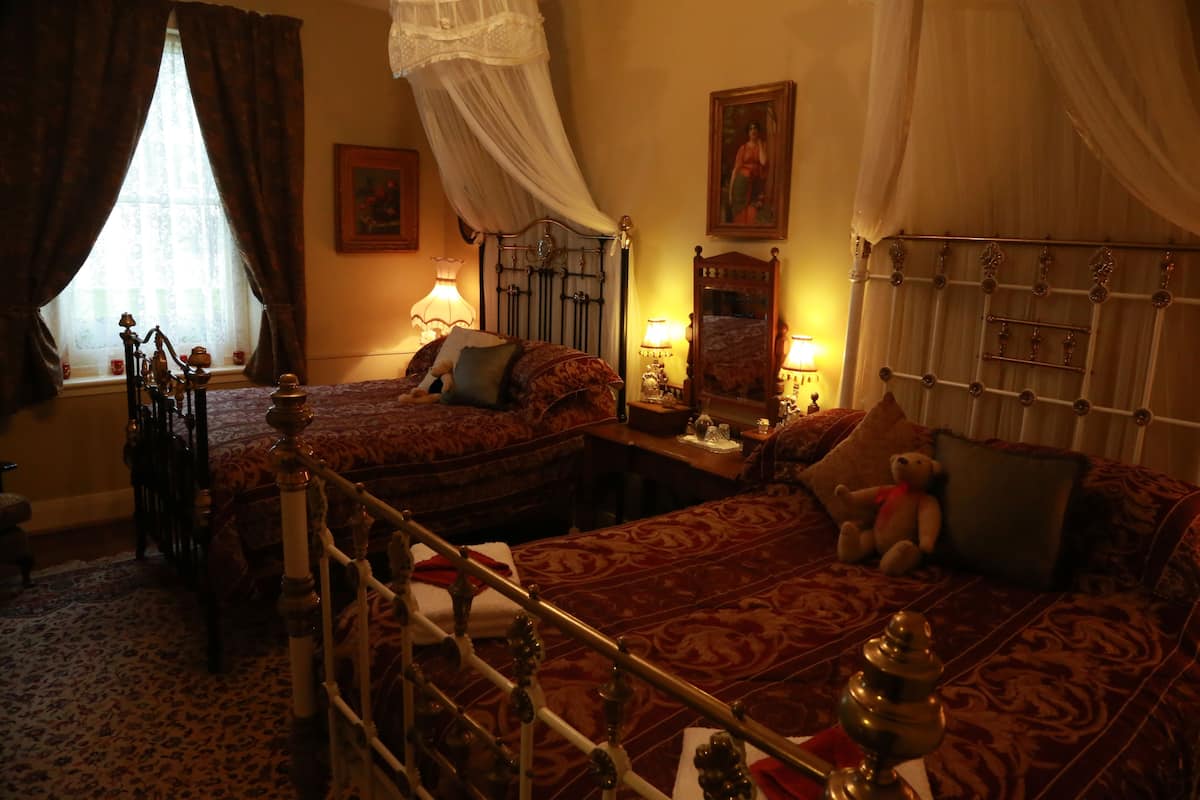 Ein traditionell eingerichtetes Schlafzimmer mit zwei Betten, einem Himmelbett und einem Nachttisch mit Lampe.