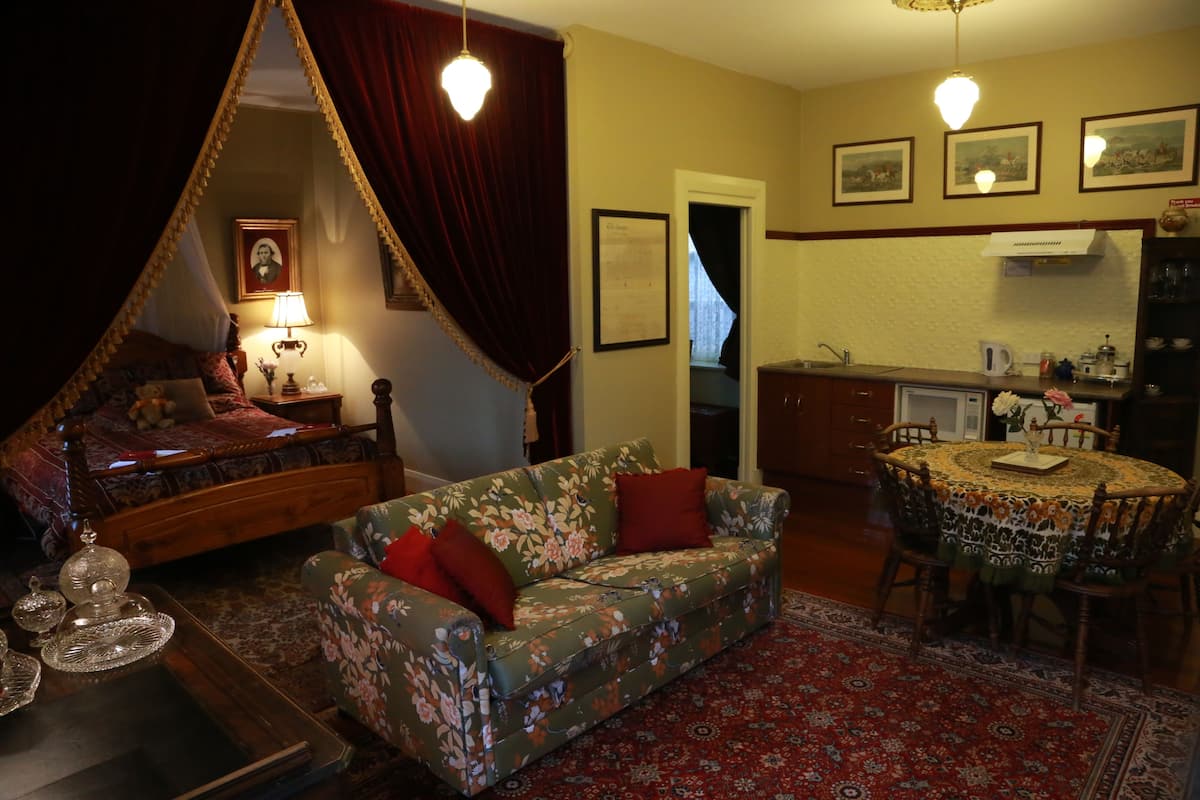 Ein Schlafzimmer mit Baldachinbett, einer blumigen Couch, einem Esstisch mit Stühlen und einer Küchenzeile.