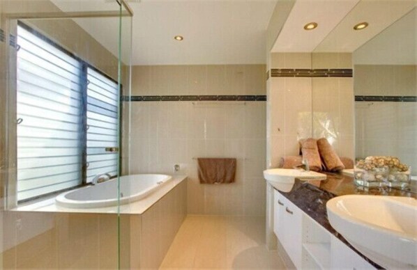 Une salle de bain moderne dotée d’une douche à parois de verre, d’une baignoire et de deux lavabos.