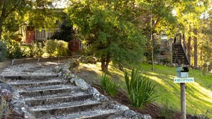 Una escalera de piedra conduce a una zona de recepción, rodeada de exuberante follaje y una valla de madera.