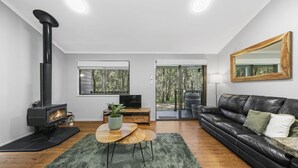 Una sala de estar moderna con un sofá de cuero negro, una mesa de centro de madera, una chimenea negra y un espejo grande en la pared.