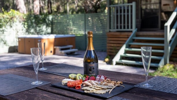 Una mesa de madera con un picnic: una botella de champán, copas y diversos aperitivos.