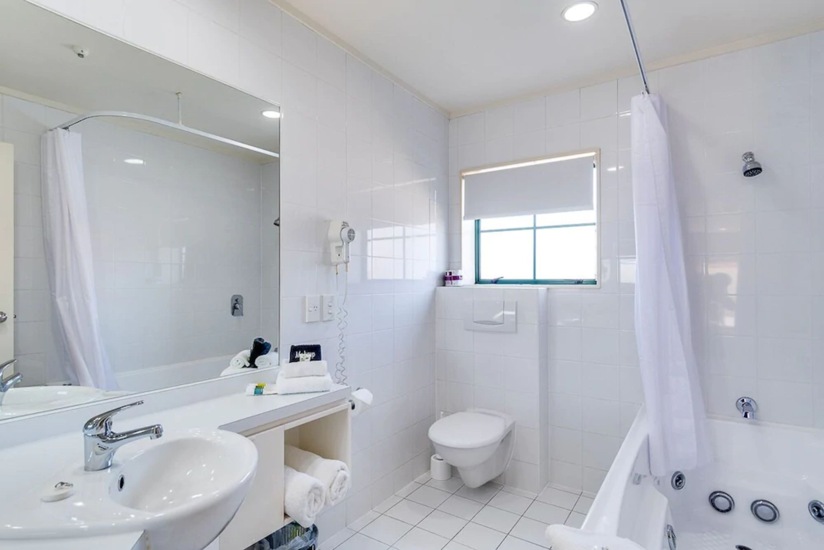 A modern bathroom with a large mirror, two sinks, a toilet, and a bathtub.