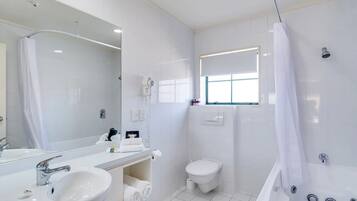 A modern bathroom with a large mirror, two sinks, a toilet, and a bathtub.