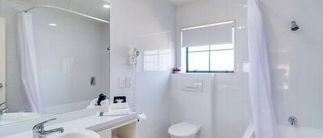 A modern bathroom with a large mirror, two sinks, a toilet, and a bathtub.
