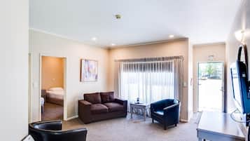 A hotel room with a bed, a brown sofa, a black armchair, a small table, and a TV.