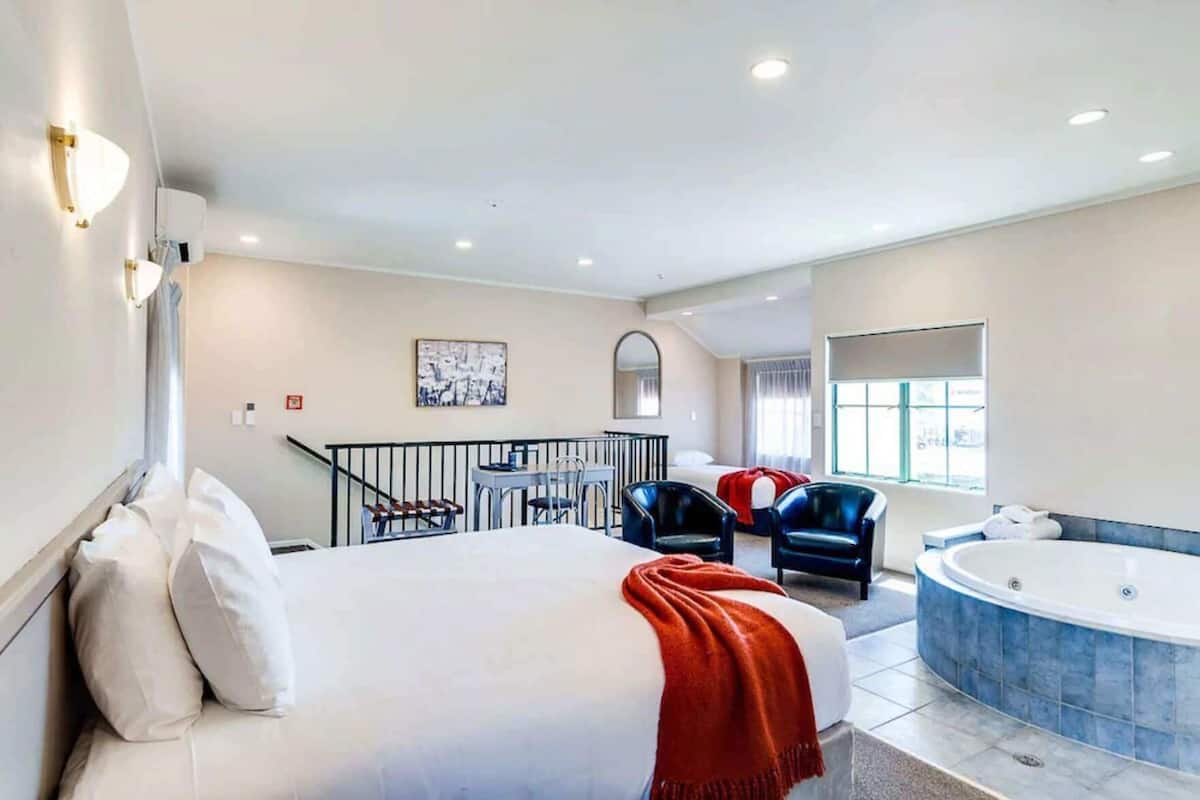 A hotel room with a large bed, a sitting area with chairs, a balcony, a jacuzzi, and a window.