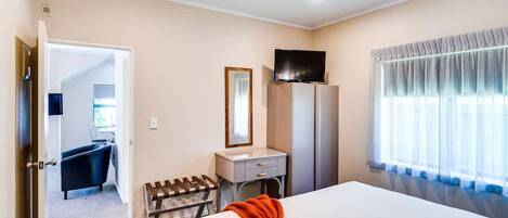 A hotel room with a bed, a desk with a chair, a television on a cabinet, and a window with curtains.