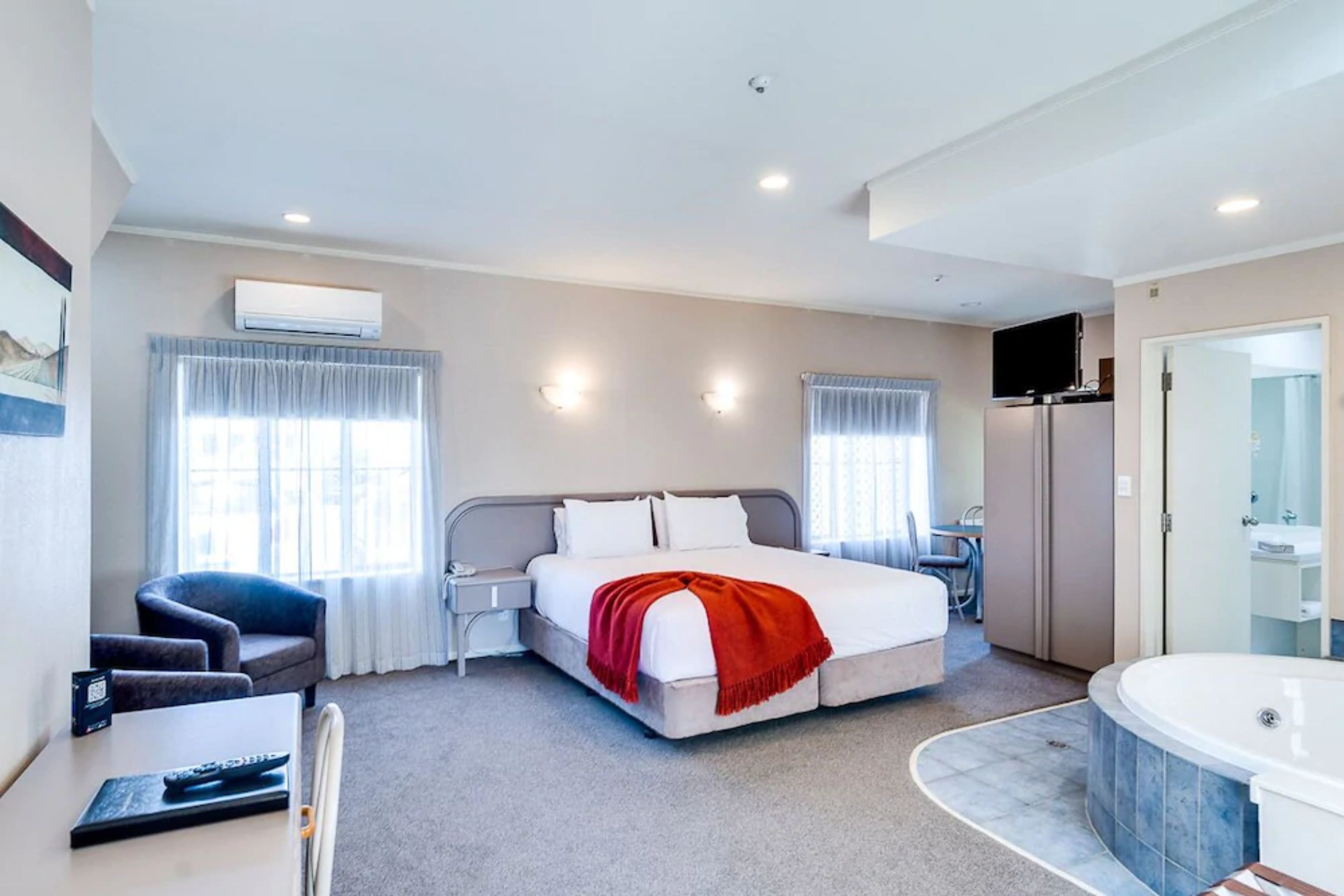 Quarto de hotel com cama, escrivaninha, cadeira, televisão, minibar e banheiro com banheira.
