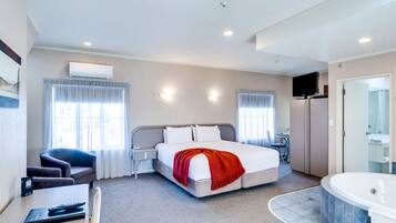 Quarto de hotel com cama, escrivaninha, cadeira, televisão, minibar e banheiro com banheira.