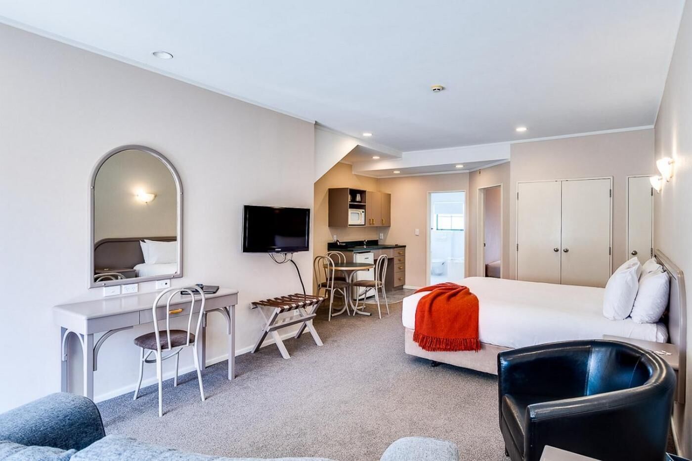 A modern hotel room with a bed, a desk, a chair, a TV, and a kitchenette.