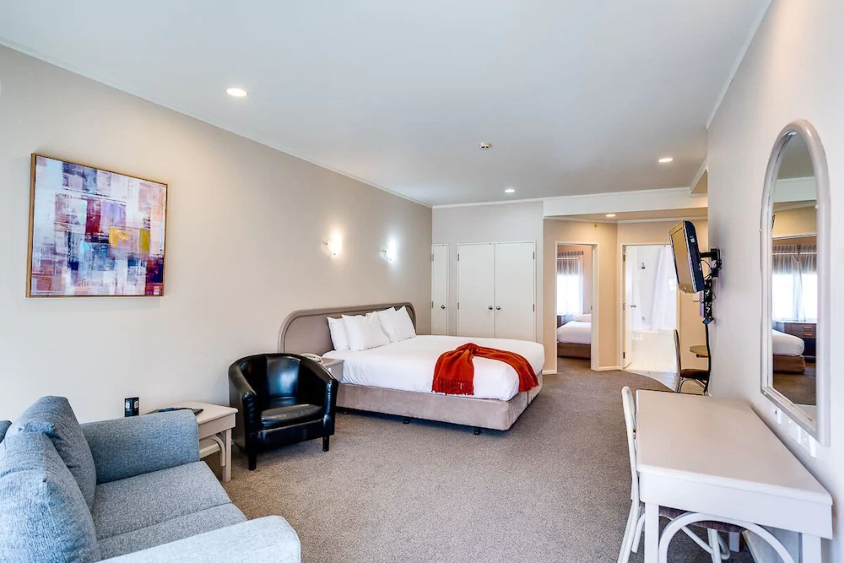 Habitación de hotel con cama, escritorio, silla, sofá y un espejo grande.