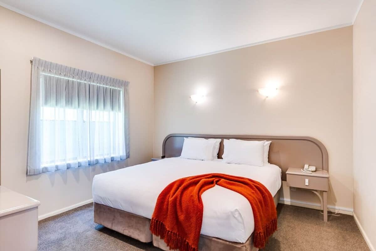 A bedroom with a bed, a nightstand, a lamp, and a window with curtains.