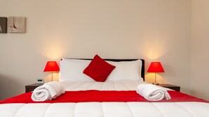 A neatly made bed with white and red bedding, two bedside lamps, and a digital clock on a bedside table. - The Park Motel (Hawera)