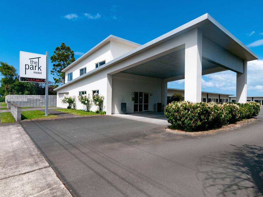 A modern motel with a covered parking area, a sign indicating vacancy, and a well-maintained lawn.
