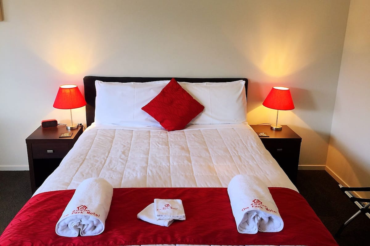 A hotel room with a neatly made bed, two bedside lamps, and a digital clock on the nightstand.