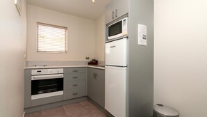 A compact kitchen with a built-in oven, microwave, and refrigerator. - The Park Motel (Hawera)