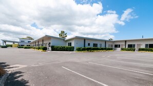 A modern building with a parking lot, a covered walkway, and neatly trimmed hedges. - The Park Motel (Hawera)