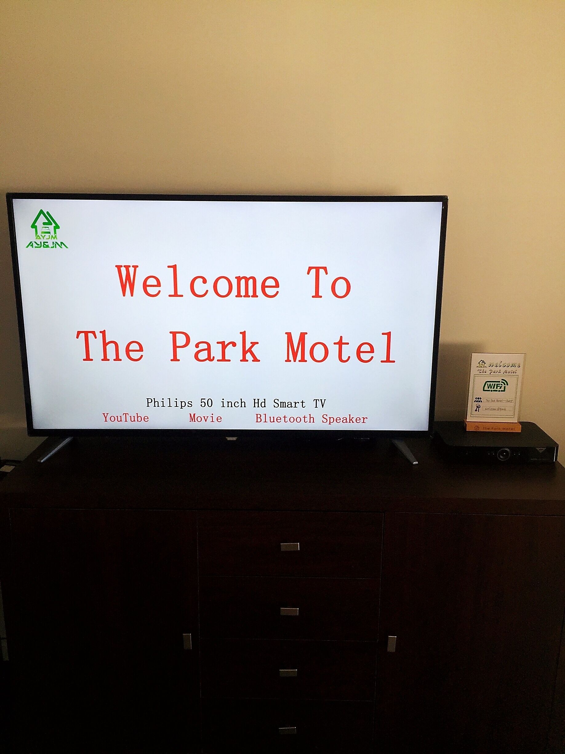 A sign welcoming guests to The Park Motel, featuring amenities like a Philips 50-inch HD Smart TV, YouTube, movie, and Bluetooth speaker.