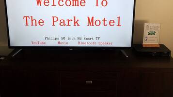 A sign welcoming guests to The Park Motel, featuring amenities like a Philips 50-inch HD Smart TV, YouTube, movie, and Bluetooth speaker.