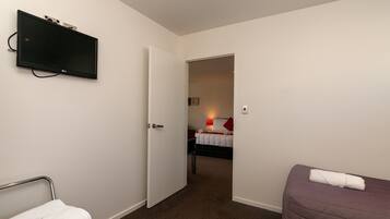 Una habitación de hotel con una cama, una mesita de noche, un televisor montado en la pared y una puerta que da a otra habitación.