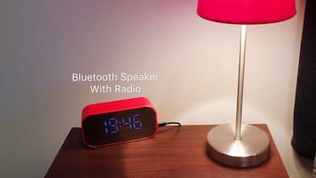 A Bluetooth speaker with a digital display on a wooden table, next to a red lamp and a sign for 'The Park Motel'.