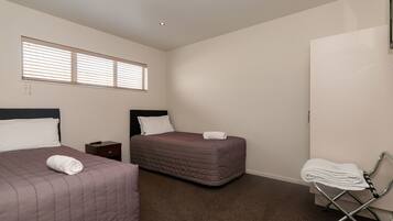 Quarto de hotel com duas camas, uma mesinha de cabeceira, uma cadeira e uma janela com persianas.