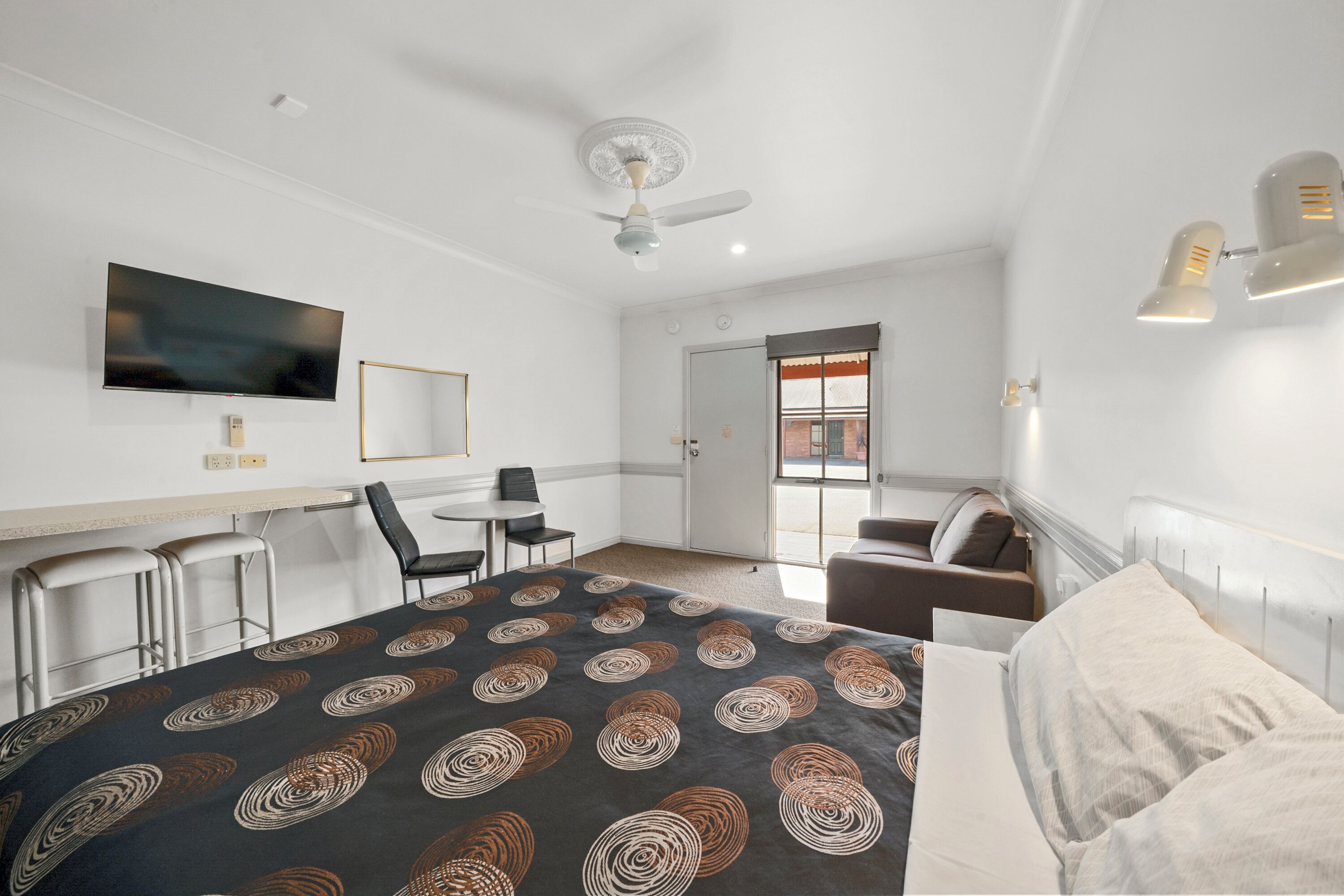 A hotel room with a bed, a desk, a chair, a television, and a ceiling fan.