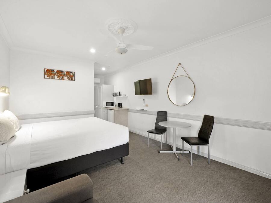 Een hotelkamer met een bed, een bureau, twee stoelen, een televisie en een plafondventilator.