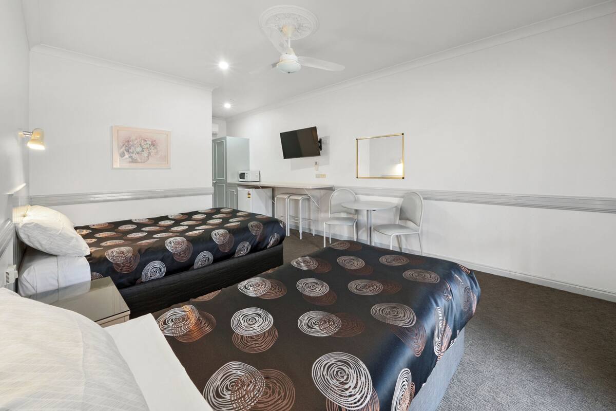 Habitación de hotel con dos camas, un escritorio, una silla, un televisor y un ventilador de techo.