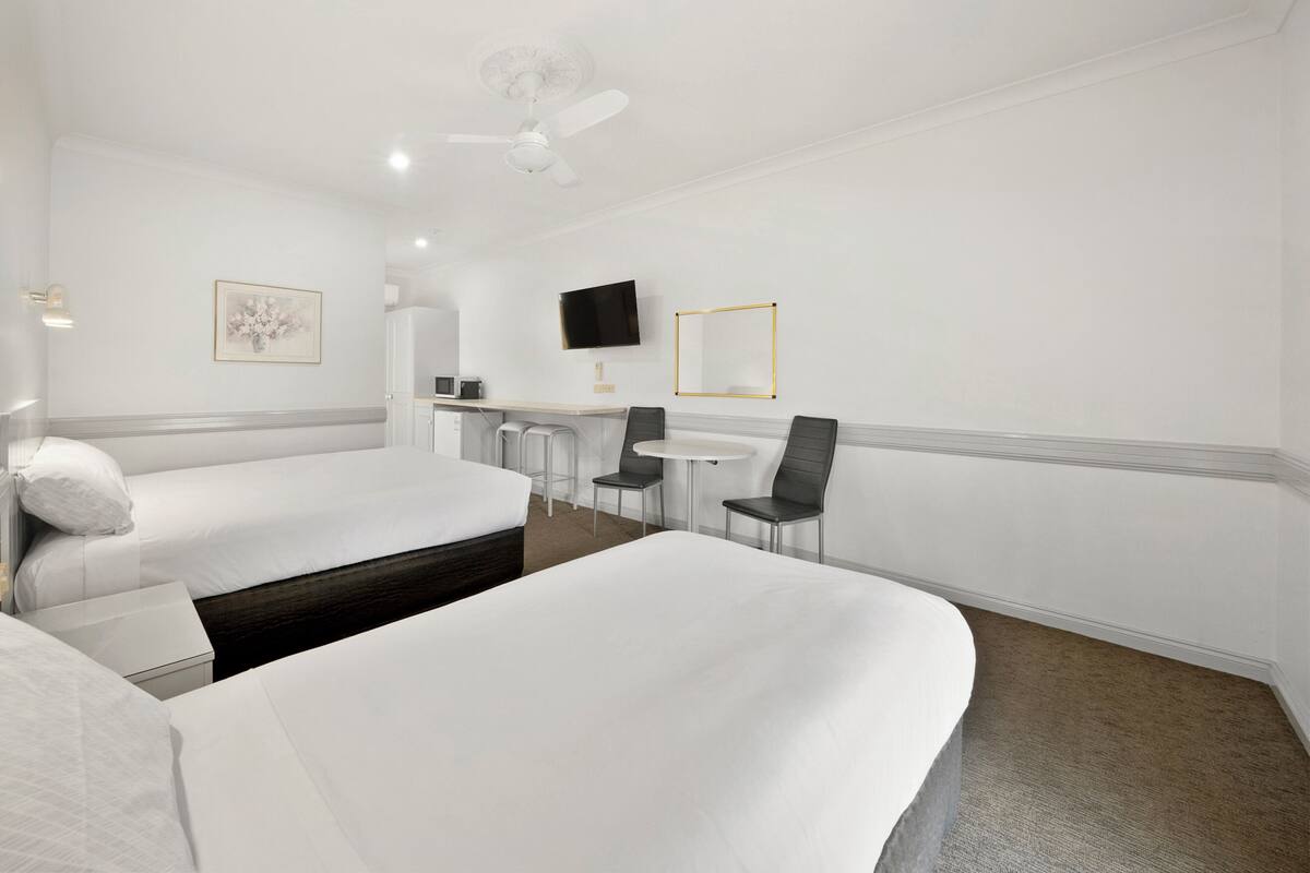 Habitación de hotel con dos camas, un escritorio, una silla, un televisor y un ventilador de techo.