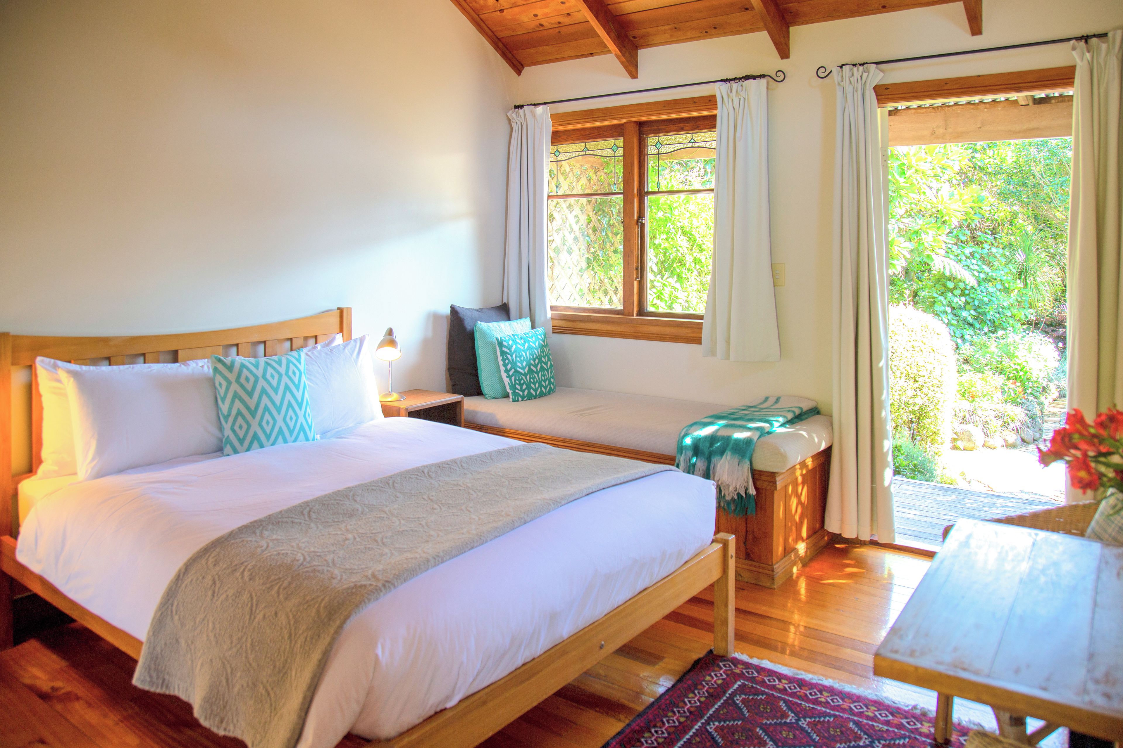 Une chambre à coucher avec un lit en bois, une table de chevet, une fenêtre avec des rideaux et une vue sur la verdure à l’extérieur.