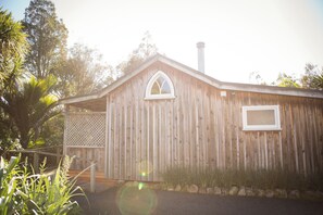 A wooden building with a pitched roof, a chimney, and a small window. - Church Accommodation (Hahei)