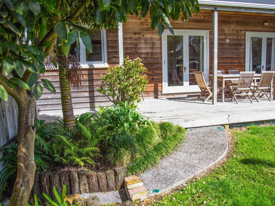 A wooden cabin with a patio, outdoor seating, and a garden area with ferns and a tree.