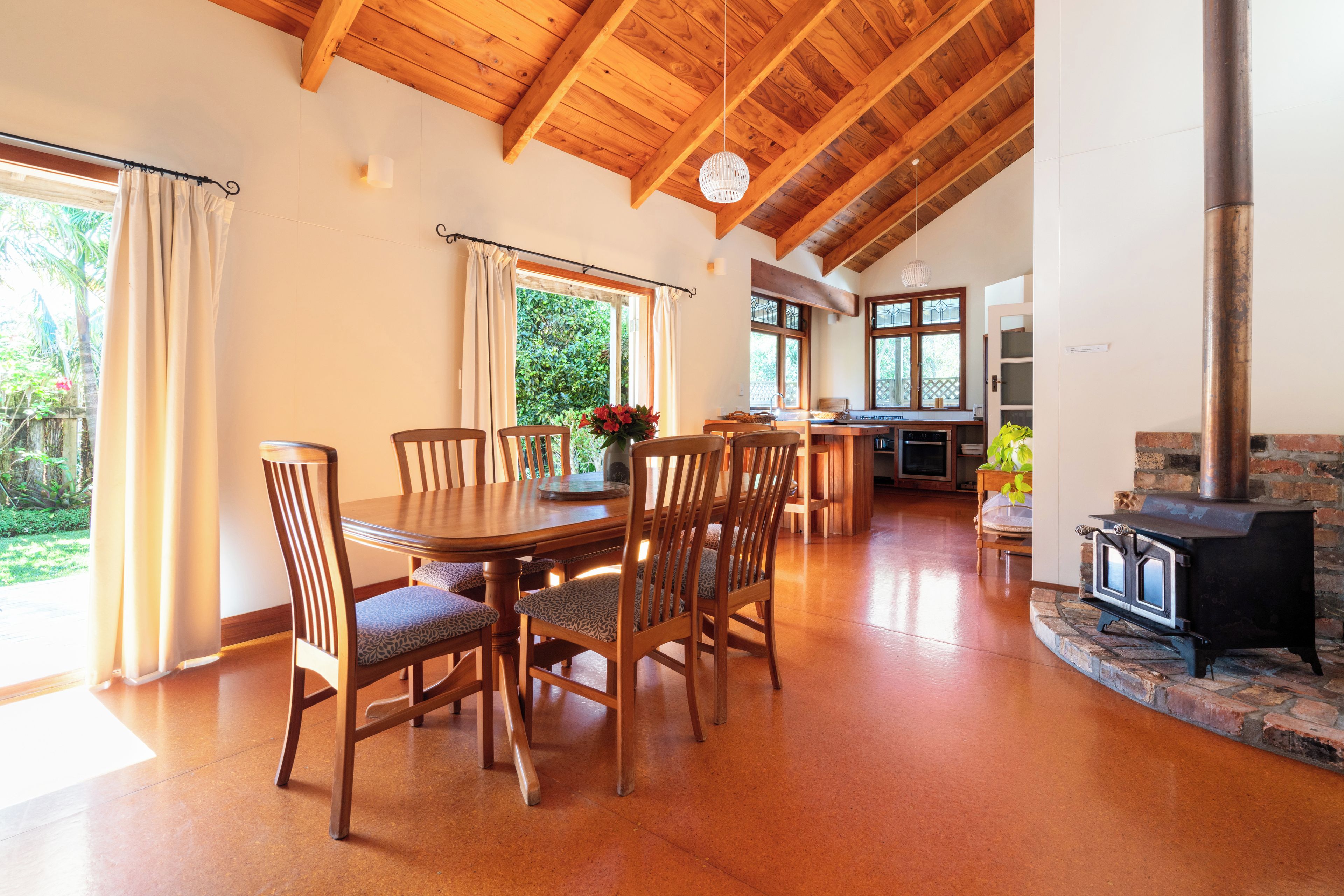A dining area with a wooden table and chairs, a kitchen in the background, and a stone fireplace.