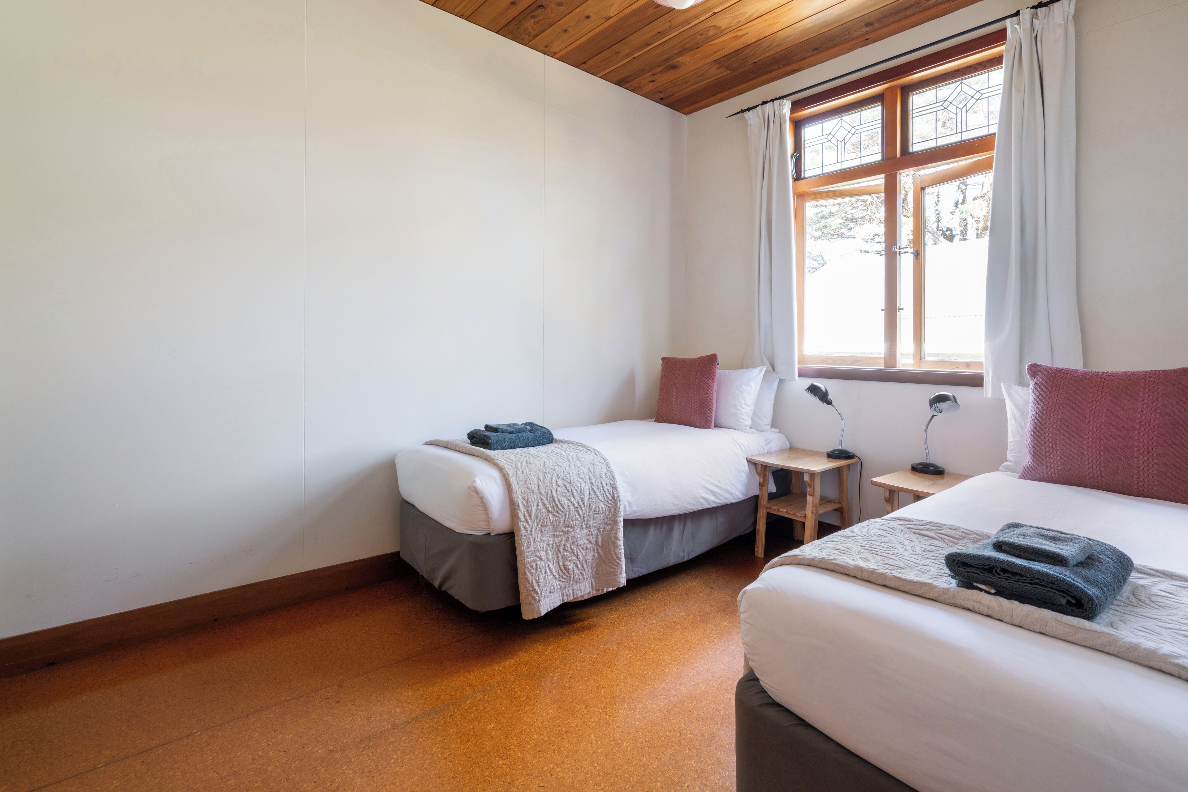 A bedroom with two beds, a window with curtains, and a wooden floor.